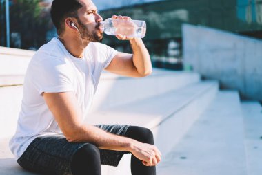 Kafkasyalı erkek sporcu sabah antrenman için şehir merkezinde soğuk suyla serinliyor. Elektronik kulaklıklı güçlü bir sporcu multimedya ses kayıtlarını dinliyor.