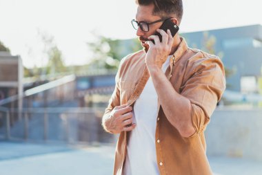 Görme düzeltmesi için optik gözlüklü beyaz bir erkek uluslararası gümrük tarifesini gezintide iletişim için kullanıyor, modaya uygun giyinmiş bir adam cep telefonu uygulaması üzerinden akıllı telefon danışmanlık görüşmesi yapıyor.