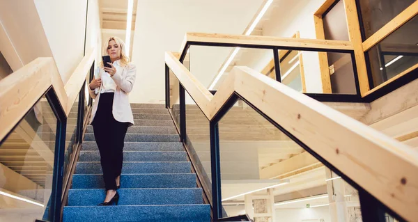 在巴塞罗那市的现代工作空间工作时 穿着正式服装的身材优雅的女士站在台阶上 浏览智能手机 — 图库照片