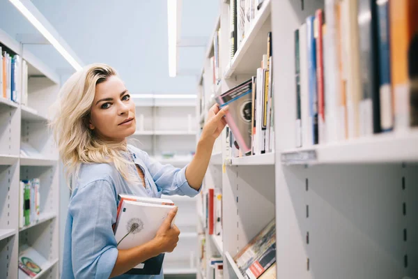 書店で買い物をするための本を選ぶ美女学生の半分の長さの肖像画 コーカサスの図書館員は 書籍ケースから文学ベストセラーを選ぶ注文を収集します — ストック写真