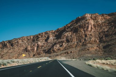 Amerika Birleşik Devletleri 'nde güneşli bir günde mavi bulutsuz gökyüzüne karşı dağlık arazide dümdüz asfalt boş bir yol.