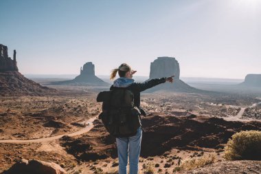 Anıt Vadisi 'nde yön gösterirken sırt çantalı ve kayanın üzerinde duran yüzü olmayan kadın turistin arkası.