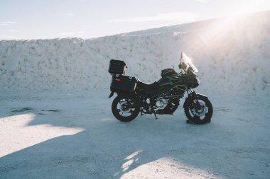 Güneşli bir günde White Sands Ulusal Parkı 'nda kumlu kum tepeciği yakınlarında boş bir yola park edilmiş siyah modern motosiklet.