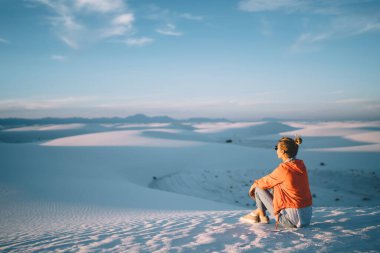 Amerika Birleşik Devletleri 'nin ulusal parkında güneşli bir günde beyaz kum tepeciklerinde dinlenen kadın spor kıyafetlerinin arka görüntüsü.