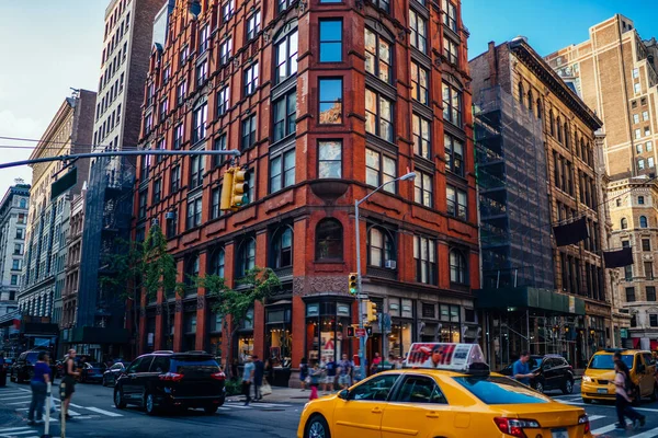 Busy street with modern cars and taxi driving on crossroad and people on crosswalk crossing street with tall old buildings above