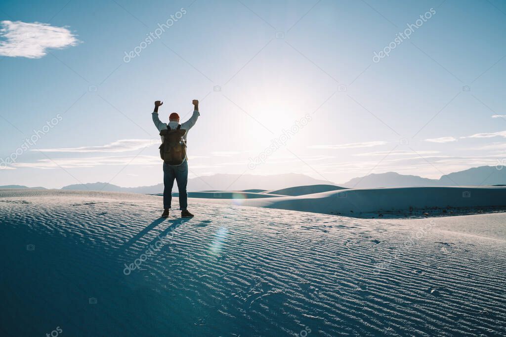 Back view of man with hands up in wide desert with white sand and bluy sky during dusk in America