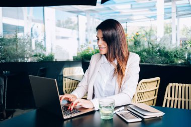 Zeki gündelik kıyafetlerde başarılı bir kadın internetten iletişim kurmaya, dizüstü bilgisayardan e-posta göndermeye, blogda paylaşım metni yazan kendine güvenen bir iş kadını kafe terasında oturuyor.