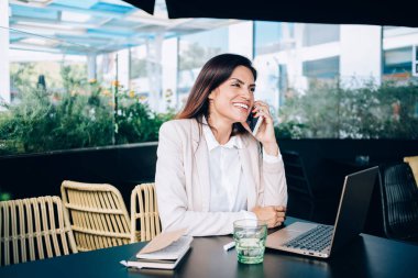 Neşeli esmer kadın, kafede uzaktan kumandalı bir iş sırasında cep telefonuyla konuşuyor. Akıllı telefondaki konuşmadan memnun. Boş zamanlarında servise çağrı yapıyor.