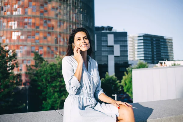 身着休闲装 面带微笑的高加索女性坐在城市背景下享受着手机对话 30多岁的积极女性则使用漫游费和连接电话 — 图库照片