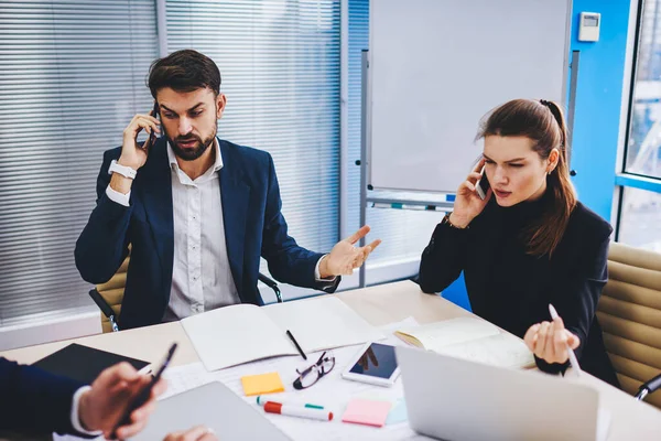 Experienced male and female bankers calling to customers for discussing mortgage deal using smartphone gadgets in office interior, Caucasian executive managers solving business problems while phoning