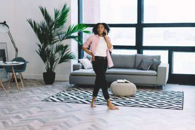 Evdeki rahat oturma odasında telefon görüşmesi yaparken cebinden dışarı bakan gündelik giysili düşünceli genç bir kadın.