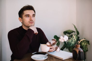 Kahve fincanı tutan dalgın esmer adam ve hafta sonu boş zamanlarında web günlüğü fikirleri hakkında düşünen, kafeterya içinde derin derin düşünen sıcak kafein içeceği içen düşünceli erkek şair.