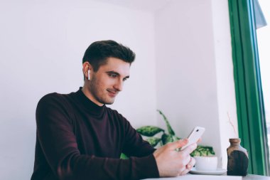 Bluetooth kulaklıklı beyaz bir adam popüler medya listesinden müzik şarkıları seçiyor ve milenyum erkeğinin kulaklık takıp internet sitesinde video bloğu izleyerek boş zamanlarını geçiriyor.