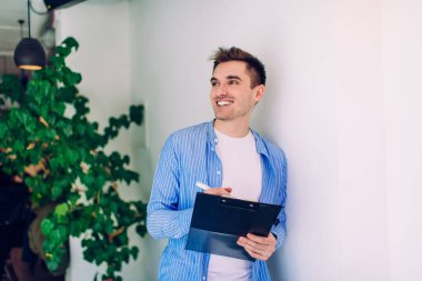 Kağıt klasörlü neşeli Kafkasyalı stajyer iş şansından memnun, üniversite projesi için ilginç fikirler üreten, organizasyon için ekipman kullanan mutlu erkek öğrenci.