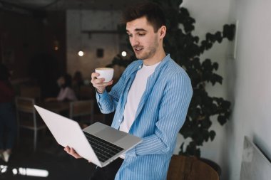 Kahve fincanı ile hayrete düşmüş erkek serbest yazar dijital dizüstü bilgisayardan gelen e-posta ile şok oldu, Kafkasyalı bir adam sosyal ağlarda web haberlerini okurken 4G internet kullanarak merak ediyor