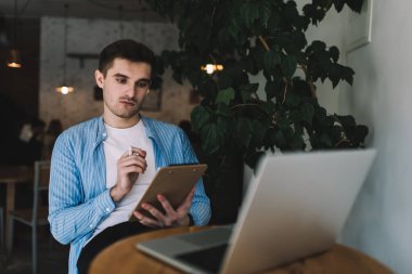 Modern dizüstü bilgisayarla aynı masada oturan ve notları kontrol eden yakışıklı, beyaz tenli metin yazarı. Uzaktan eğitimli bir erkek analiz raporu ve netbook 'tan öğrenme.