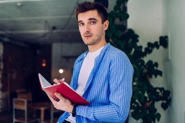 İyi görünümlü bir erkek öğrencinin yarım boy portresi. Eğitim bilgisi için kitap yazıyor. Kameraya bakıyor.