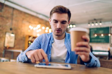 Medya uygulaması için online bankacılık yapan elektronik kulaklıklı bin yıllık Kafkasyalı kullanıcı, kafeteryada boş zamanlarında dinlemek için ses kitabı aramak üzere kahve getiren genç Y jenerasyonu.