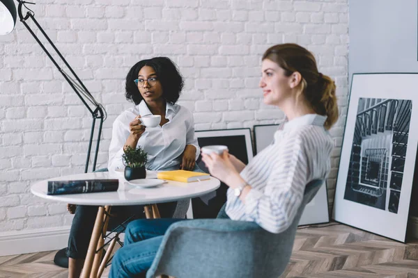 Zufriedene Frauen Lässiger Kleidung Trinken Kaffee Und Plaudern Während Sie — Stockfoto