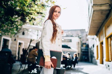 Barcelona caddesinin bulanık arka planında, açık kafenin yanında durup kameraya bakıp gülümseyen neşeli genç bayanın yan görüntüsü.