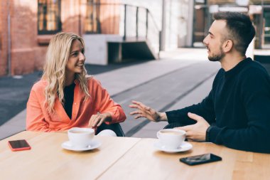 Pozitif genç erkek ve bayan meslektaşlar kafeteryanın terasında oturmuş boş zamanlarında iletişim kuruyor, beyaz kadın ve erkek kahve içerek eğleniyorlar.