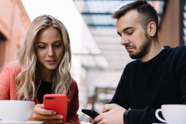Uzun saçlı, ekran kadınına odaklanmış ve gündüzleri kafede kahve içerken akıllı telefon kullanan, günlük kıyafetli, sakallı bir adama kızmış.