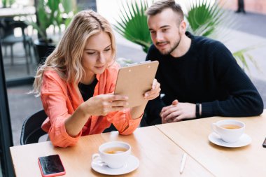 Odaklanmış bir adam ve kadının masada oturup panoda notlar okuması ve sokak kafesinde uzaktan bir proje üzerinde çalışması.