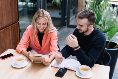 Neşeli beyaz kadın ve erkek öğrenciler proje planlama fikirlerini tartışıyor birlikte vakit geçirmekten keyif alıyor bilgileri kontrol ediyor, kafe terasında çalışan gülümseyen kadın çalışanlar notlar alıyor.