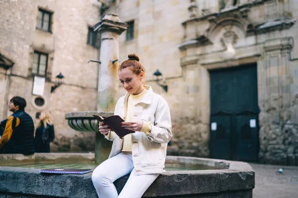 バルセロナ市内の通りで勉強しながら 古い噴水の近くに座ってメモ帳を読んでスタイリッシュな衣装を着たかなり若い女性 — ストック写真