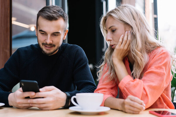 Жуткая белая женщина смотрит видео на смартфоне своего бойфренда, используя 4G соединение, 20-летний юноша, показывающий фото на своем мобильном телефоне своей девушке, сидящей в кафе вместе