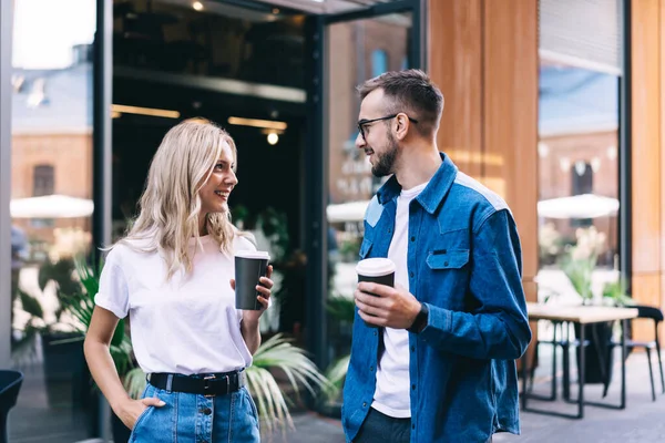 コーヒーを飲みながら会話を楽しみながら笑顔でモダンなストリートカフェの近くでお互いを見ている肯定的な若いカップル — ストック写真