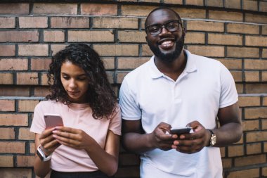 Kız arkadaşıyla kameraya gülümseyen neşeli Afrikalı Amerikalı erkek blog yazarının yarım boy portresi. İnternette gezen çekici hippi kız mutlu adamı görmezden geliyor.