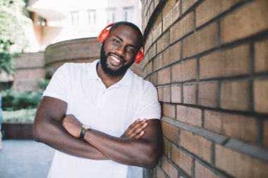 Elleri çaprazlı koyu tenli bir adam boş zamanlarında kulaklıkla popüler şarkıların tadını çıkarıyor. Elektronik teçhizatla sesi dinleyen Afrikalı Amerikalı hippi adamın yarım boy portresi.