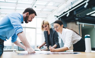 Şık giyinen, hafif gülüşlü, büyük kağıt üzerine fosforlu kalemler çizen bir grup iş arkadaşı.