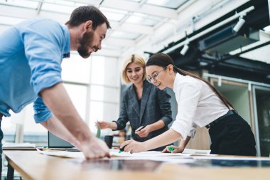 Ceketli neşeli sarışın kadın, gözlüklü, gözlüklü, gülümseyen kadın meslektaşının mavi gömlekli, sakallı bir erkeğin karşısında nasıl iz bıraktığını izliyor.
