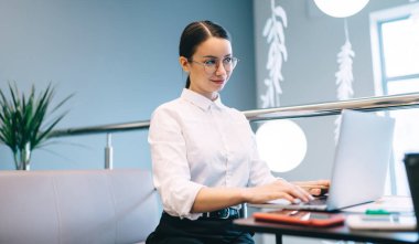 Düşük açılı, iş elbiseleriyle kafede çalışan, dizüstü bilgisayarlı ve akıllı telefonlu genç ve çekici bir bayan yönetici. Klavyeye yazı yazıp, cilveli bakışlarını kaçırıyor.