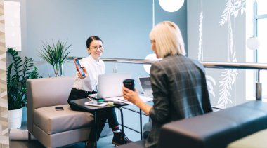 Genç ve mutlu bayan meslektaşlar, kafeteryada dizüstü bilgisayar ve gazetelerle otururken keyifle konuşuyorlar. Kâğıt bardaktan kahve içiyorlar, akıllı telefon ekranları ve gülümsüyorlar.