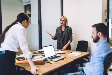 Masada karşı karşıya duran iki bayan meslektaşım düşünceli bir adam ofiste dizüstü bilgisayarlı ve kağıtlı bir şekilde otururken iş projesinden bahsediyorlar.