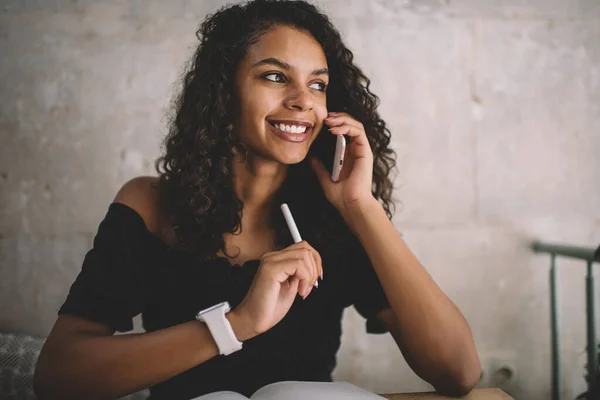快乐的黑皮肤卷曲的女性在手机上谈论室内商业规划 微笑的20多岁的美国嬉皮士女孩拿着手机记笔记 — 图库照片
