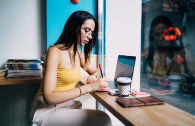 Klasik gözlüklü yetenekli bir kadın metin yazarı, modern netbook bilgisayarında 4G kablosuz internete bağlanırken aynı zamanda gözlüklü Kafkas hippi kız da uzaktan çalışıyor.