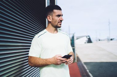 Seyyar teknolojisi olan düşünceli bir erkek koşucu. Düşünceli bakışlar atıyor ve spor sonuçlarını düşünüyor. Hücresel cihazları olan düşünceli bir sporcu.