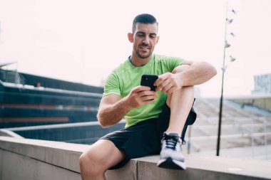 Kafkas erkek atlet, sabah kardiyo eğitimi için spor sonuçlarını analiz etmek için cep telefonu uygulamasını kullanıyor. İnternete bağlanan kaslı adam internet üzerinden web çalışması yapıyor.