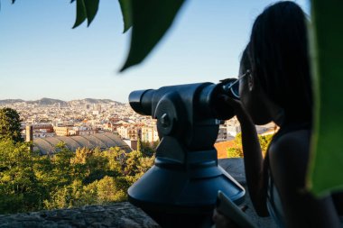 Gözlüklü, siyah saçlı, turistik panoramik dürbünlerden bakıp güneşli bir günde görüş açısında duran tanınamaz bir kadının arka görünüşü.