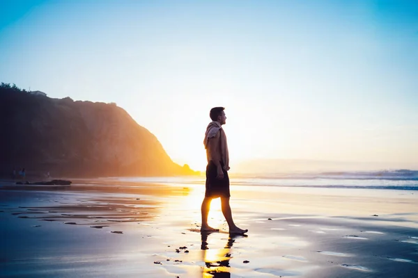 穏やかな海に近い朝の日の出の景色を楽しむ男性旅行者のシルエット 岩や海辺の海岸近くに立つヒップスター男旅行者オレンジの夜の夕暮れの空を見て — ストック写真