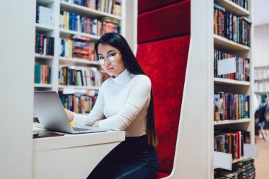 Kameraya bakarak çağdaş kütüphane bireysel alanında sınav hazırlıkları sırasında gözlüklü Asyalı genç esmer.