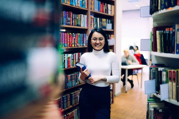 Счастливая Азиатская Студентка Очках Голубой Книгой Руках Стоящей Проходе Между — стоковое фото