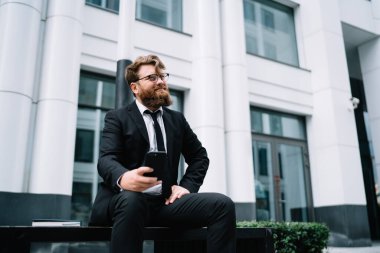 Resmi kıyafetleri ve şık gözlükleri olan düşünceli sakallı işadamlarının oturduğu bankta otururken ve akıllı telefonları karıştırırken