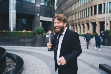 Ofis için takım elbiseli neşeli genç erkek işçi şehir parkında mola verirken podcast dinlemek için tablet ve kulaklık kullanıyor.