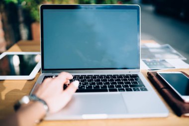 Kol saatli isimsiz kadın serbest yazar açık kafedeki ahşap masada oturur ve güneşli bir günde dizüstü bilgisayarda klavye çalar.