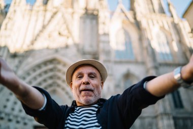 Yaşlı beyaz nüfuzlu 60 yaşında, tarihi şehri keşfetmek için solo yolculuk sırasında seyahat vlog 'u çekiyor. Hasır şapkalı yaşlı erkek turist, gezi sırasında kendini fotoğraflıyor.